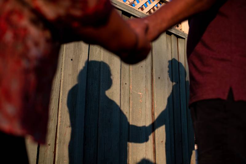 Two people hold hands with late afternoon orange sunlight creating a shadow of the two people on the fence behind them.