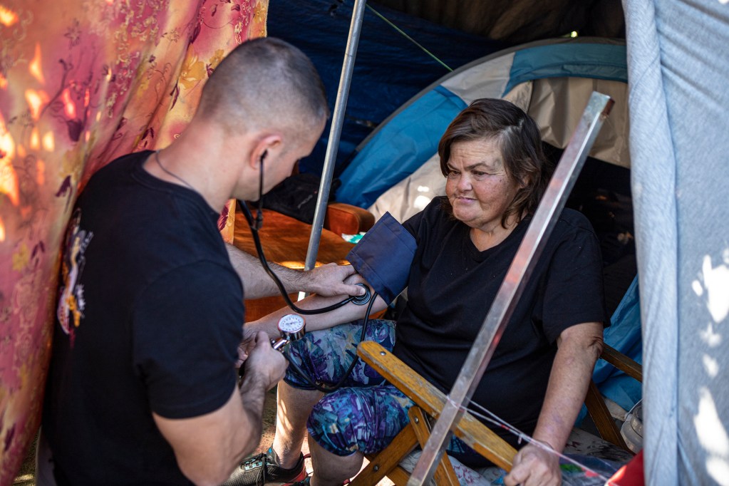 Physician assistant Brett Feldman checks his patient, Carla Bolen’s, blood pressure while in her encampment at the Figueroa St. Viaduct above Highway 110 in Elysian Valley Park in Los Angeles on Nov. 18, 2022. Photo by Larry Valenzuela, CalMatters/CatchLight Local