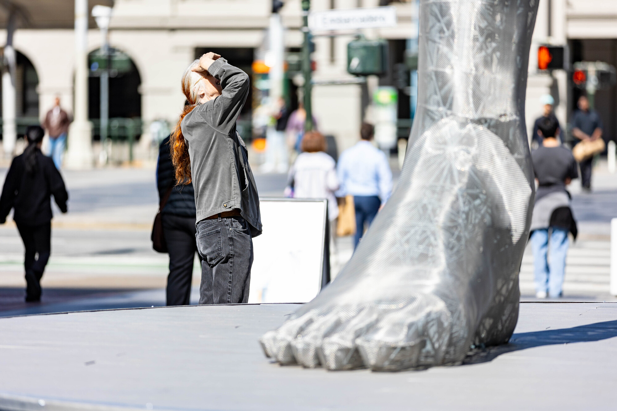 person shades eyes and looks up next to giant metal mesh foot