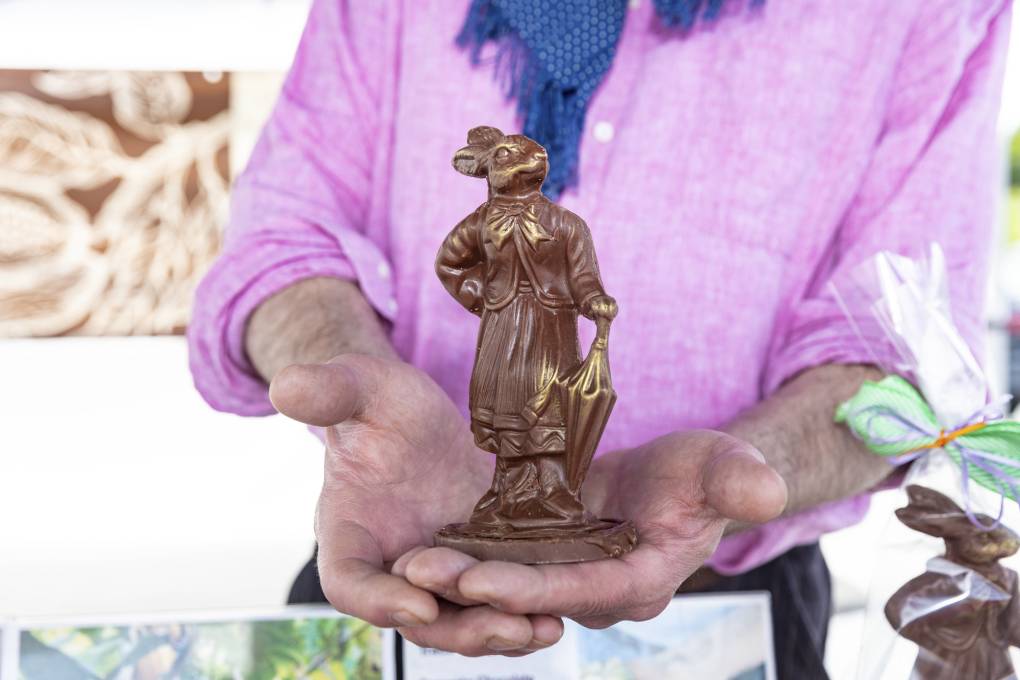 An elaborately detailed chocolate bunny held by a man in a pink linen shirt.