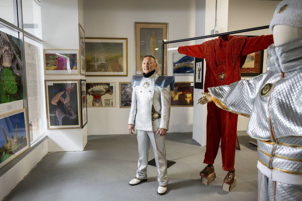older man in silver outfit stands within gallery space filled with art and fashion