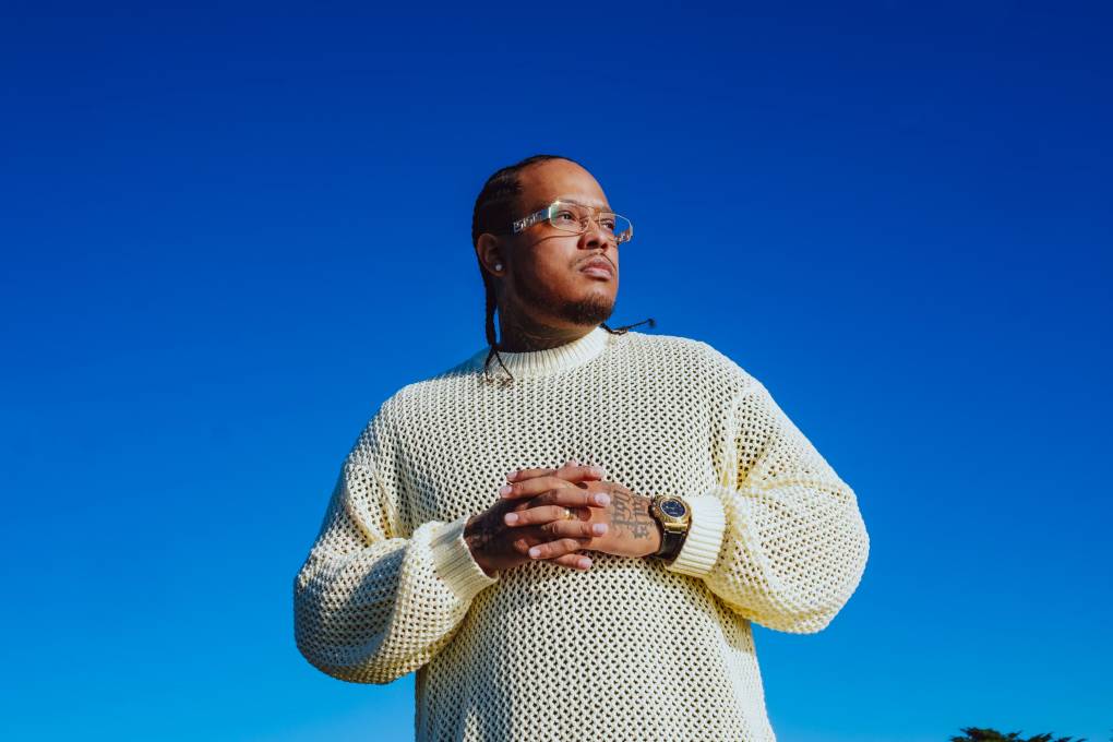 A man in a white sweater, hands together, looking off the camera while wearing glasses.